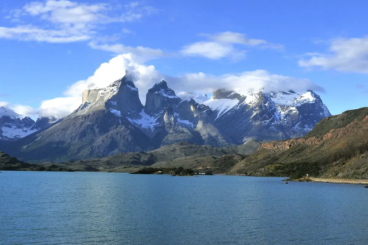 The Cuernos del Paine, dark granite peaks streaked with snow and wrapped in cloud, rising above the blue water of Lago Pehoé